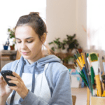 Lady using her phone for finances in front of an easel