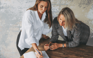 A business coach and their client at a desk reading a document.